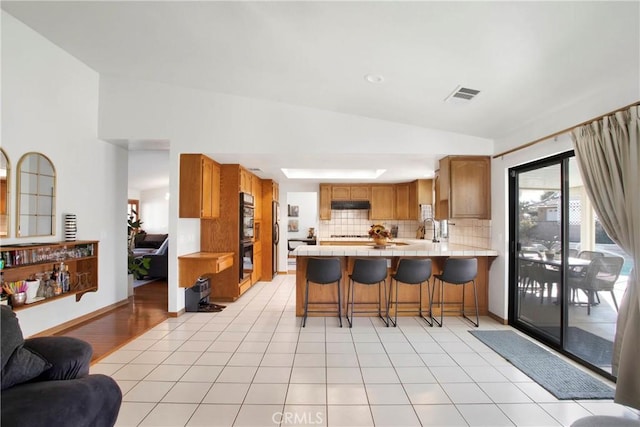 kitchen with sink, tasteful backsplash, kitchen peninsula, lofted ceiling, and a kitchen bar