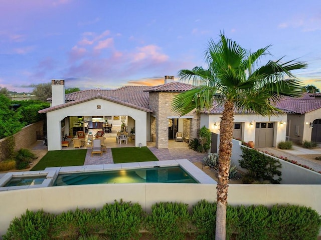 back house at dusk featuring a pool with hot tub and a patio