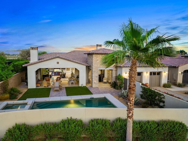 back house at dusk featuring a swimming pool with hot tub and a patio