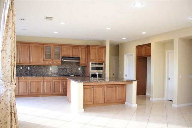 kitchen with double oven, dark stone counters, backsplash, light tile patterned floors, and black electric cooktop