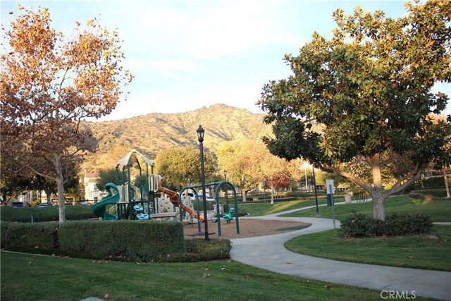 view of property's community featuring a playground, a mountain view, and a lawn