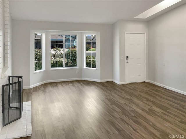 unfurnished living room featuring dark wood-type flooring, a fireplace, and a skylight