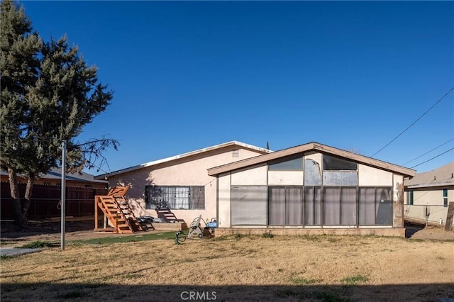 rear view of property featuring a lawn, fence, and stucco siding