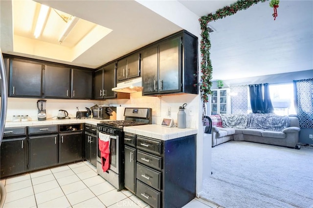 kitchen featuring tile countertops, dark brown cabinets, gas stove, and light carpet