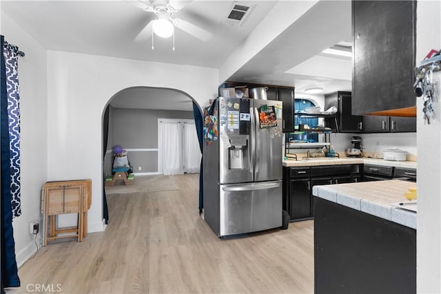 kitchen with arched walkways, tile counters, visible vents, light wood-style floors, and stainless steel fridge