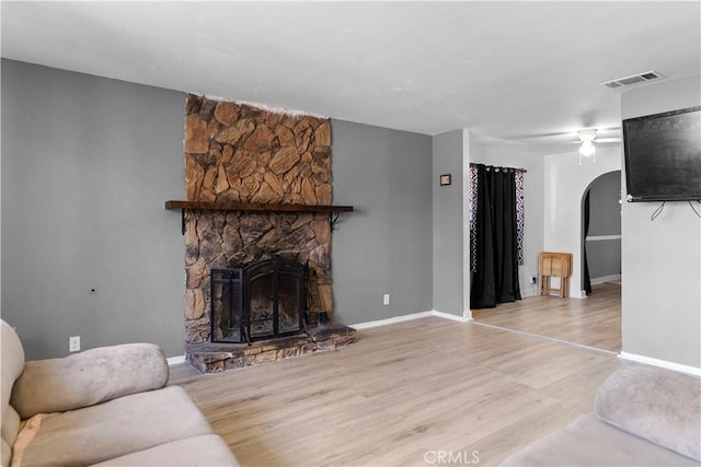 living room featuring arched walkways, a fireplace, visible vents, baseboards, and light wood-style floors