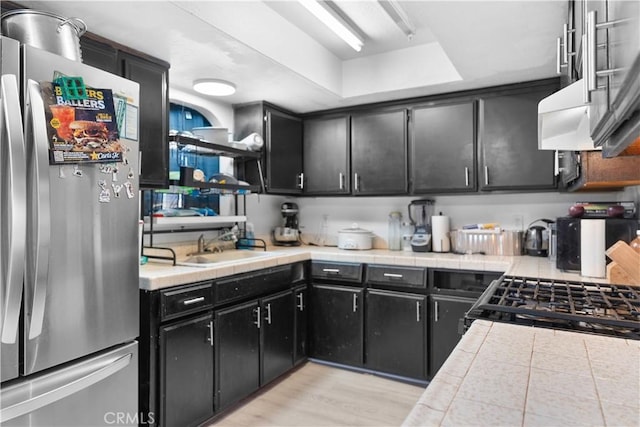 kitchen with dark cabinets, a sink, light wood-style floors, tile counters, and freestanding refrigerator