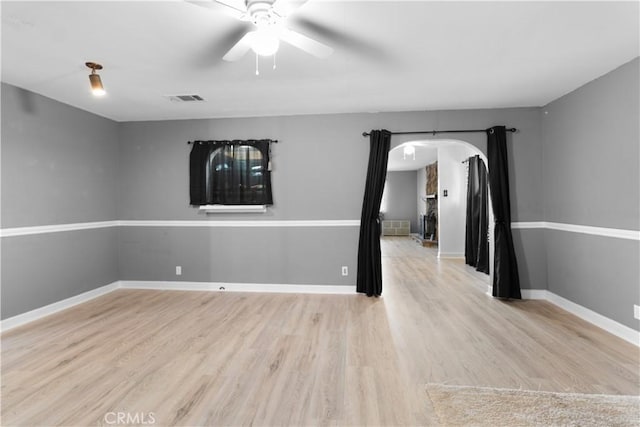 spare room featuring light wood finished floors, baseboards, visible vents, arched walkways, and ceiling fan