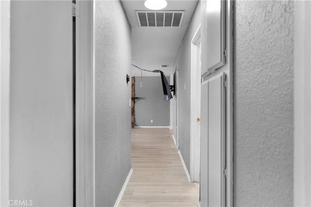 hallway featuring visible vents, a textured wall, light wood-style flooring, and baseboards