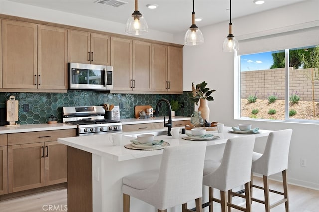 kitchen with sink, light hardwood / wood-style flooring, decorative backsplash, an island with sink, and stainless steel appliances