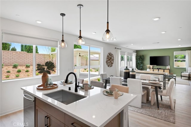 kitchen featuring sink, dishwasher, pendant lighting, light hardwood / wood-style floors, and a kitchen island with sink