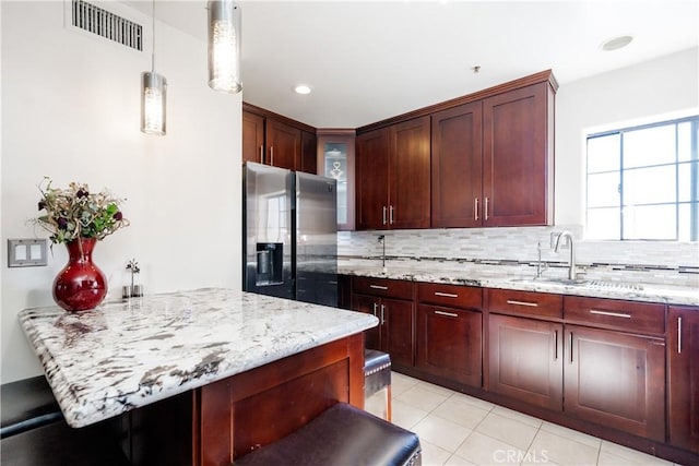 kitchen featuring decorative backsplash, stainless steel fridge with ice dispenser, pendant lighting, and light stone counters