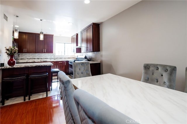 kitchen with decorative backsplash, light stone counters, decorative light fixtures, light hardwood / wood-style flooring, and stainless steel range oven