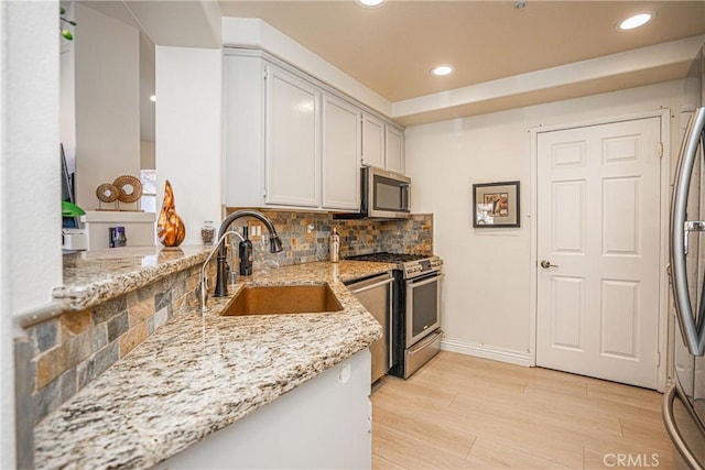 kitchen featuring sink, white cabinetry, stainless steel appliances, light stone counters, and light wood-type flooring