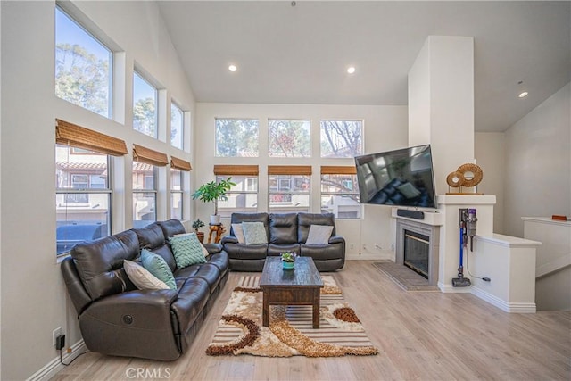 living room featuring a tiled fireplace, high vaulted ceiling, and light hardwood / wood-style floors