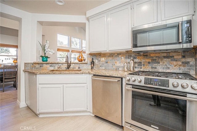 kitchen with stainless steel appliances, white cabinetry, light stone countertops, and sink