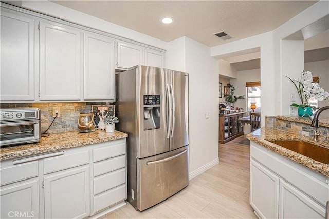 kitchen with stainless steel refrigerator with ice dispenser, sink, light stone counters, decorative backsplash, and white cabinets