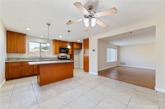 kitchen with light tile patterned flooring, hanging light fixtures, light stone countertops, stainless steel stove, and a center island