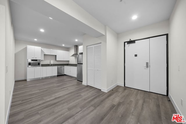 kitchen featuring white cabinetry, sink, wall chimney exhaust hood, stainless steel appliances, and light hardwood / wood-style flooring