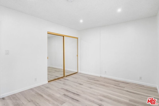 unfurnished bedroom featuring a textured ceiling, light hardwood / wood-style flooring, and a closet