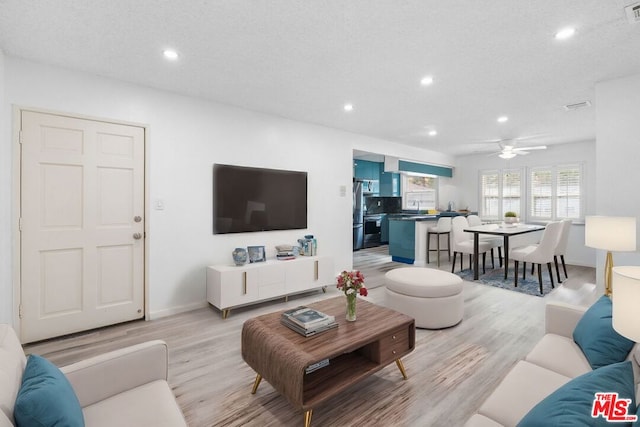 living room featuring ceiling fan, a textured ceiling, and light wood-type flooring