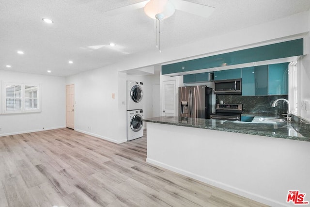 kitchen featuring light wood-type flooring, blue cabinetry, stacked washer / drying machine, kitchen peninsula, and stainless steel appliances