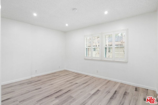 spare room with light wood-type flooring and a textured ceiling