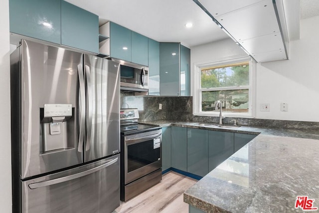 kitchen featuring blue cabinetry, sink, dark stone counters, light hardwood / wood-style floors, and appliances with stainless steel finishes