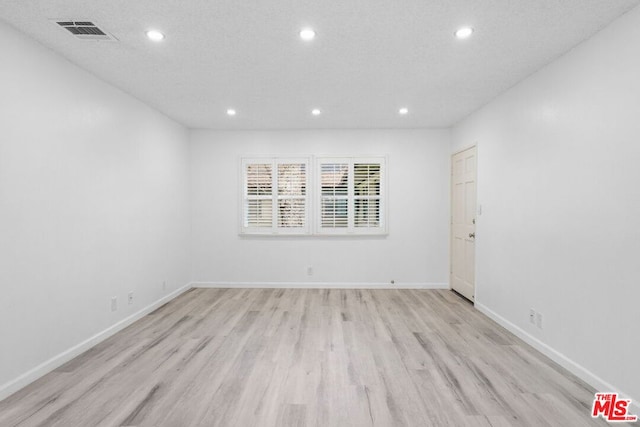 unfurnished room with a textured ceiling and light wood-type flooring