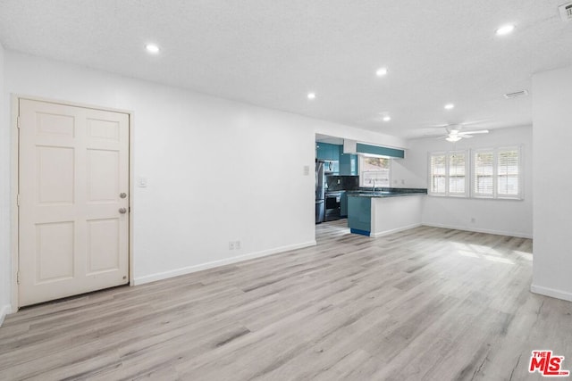 unfurnished living room featuring ceiling fan, sink, light hardwood / wood-style floors, and a textured ceiling