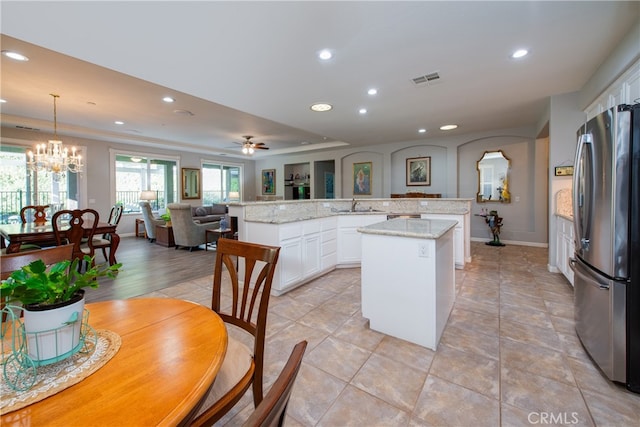 kitchen featuring pendant lighting, a center island, white cabinets, ceiling fan with notable chandelier, and stainless steel refrigerator