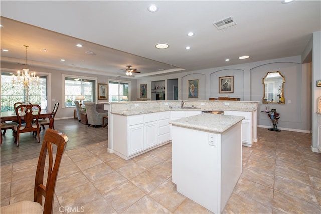 kitchen with a center island, white cabinets, ceiling fan with notable chandelier, light stone countertops, and decorative light fixtures