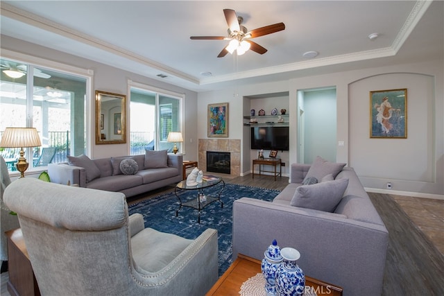 living room featuring a tile fireplace, dark hardwood / wood-style flooring, a tray ceiling, and ceiling fan