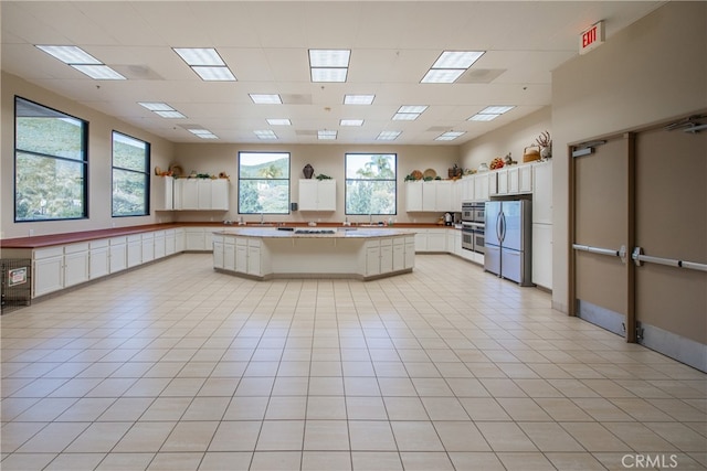 kitchen with white cabinets, a kitchen island, light tile patterned flooring, and stainless steel appliances