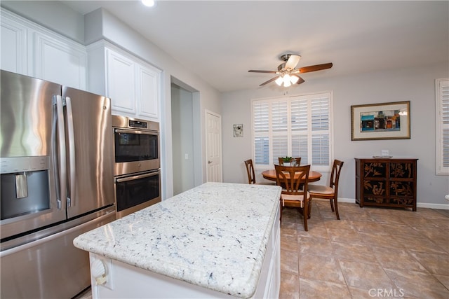 kitchen with appliances with stainless steel finishes, light stone counters, a kitchen island, ceiling fan, and white cabinetry