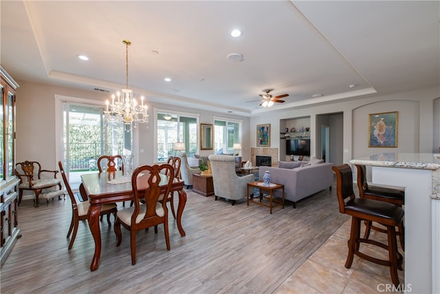 dining room with a raised ceiling, light hardwood / wood-style flooring, and ceiling fan with notable chandelier