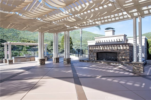 view of patio / terrace featuring an outdoor stone fireplace, a mountain view, and a pergola