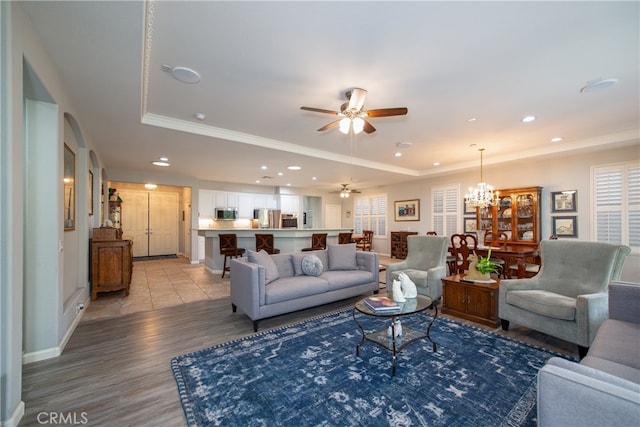 living room with ceiling fan with notable chandelier, a tray ceiling, and light hardwood / wood-style floors