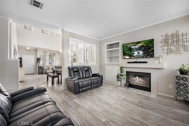 living room featuring light wood-type flooring, built in features, crown molding, and a tiled fireplace