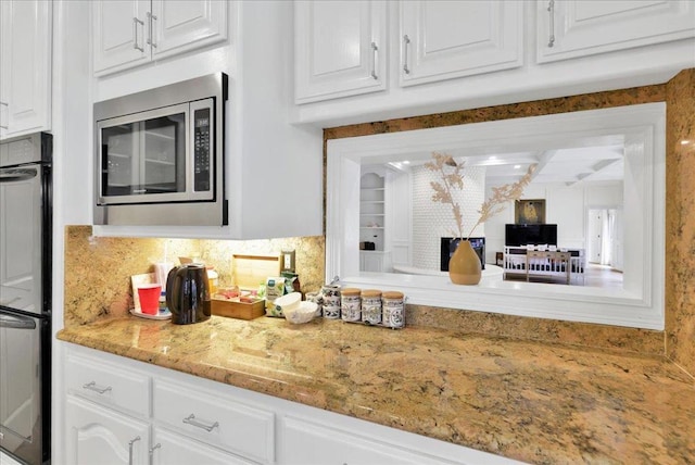 kitchen with light stone countertops, white cabinets, double wall oven, tasteful backsplash, and stainless steel microwave