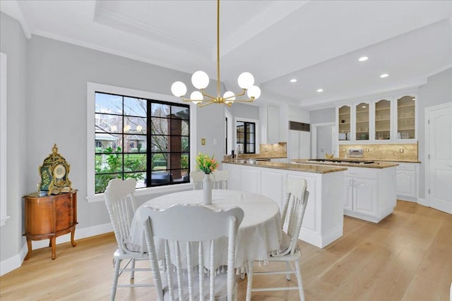 dining area featuring ornamental molding, a tray ceiling, a chandelier, and light hardwood / wood-style floors