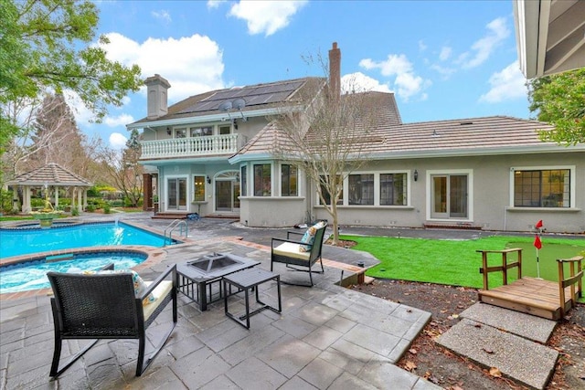 rear view of property featuring an outdoor fire pit, solar panels, a balcony, a gazebo, and a patio