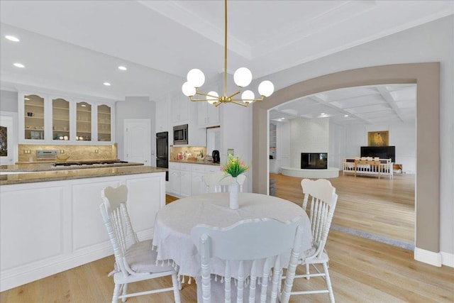 dining area with a fireplace, light hardwood / wood-style floors, an inviting chandelier, beam ceiling, and coffered ceiling