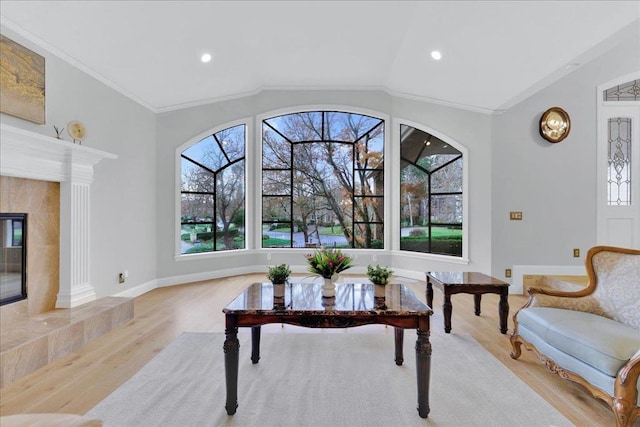 living area with vaulted ceiling, a fireplace, ornamental molding, and light hardwood / wood-style floors