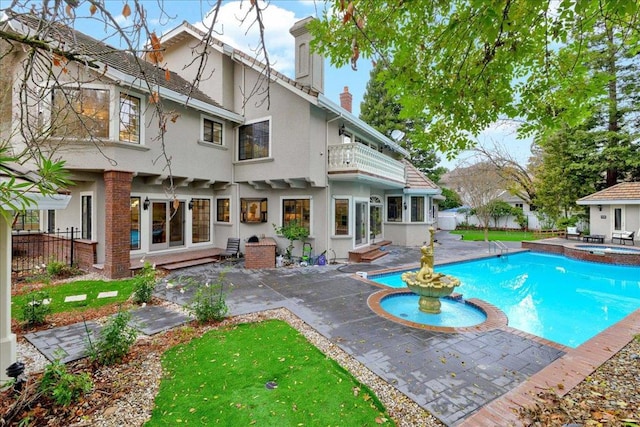 rear view of property featuring an in ground hot tub, a patio area, and a balcony