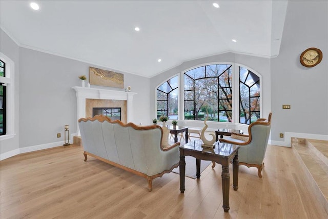 living room featuring light hardwood / wood-style floors, ornamental molding, lofted ceiling, and a tiled fireplace