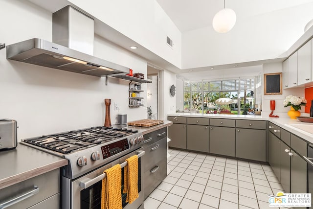 kitchen with wall chimney range hood, gray cabinets, high end stove, light tile patterned floors, and decorative light fixtures