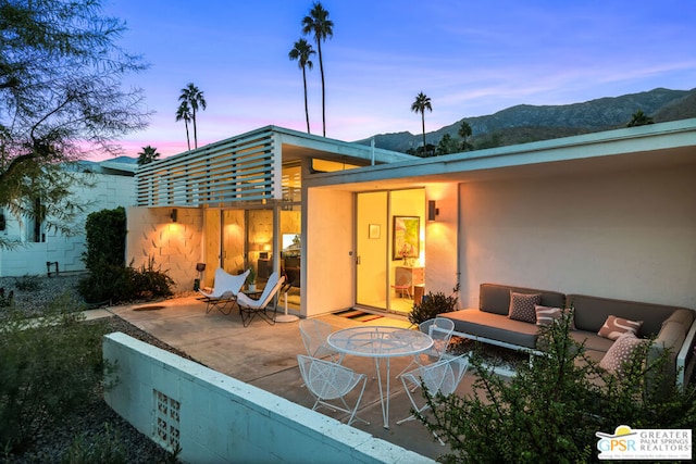 back house at dusk featuring outdoor lounge area, a mountain view, and a patio area