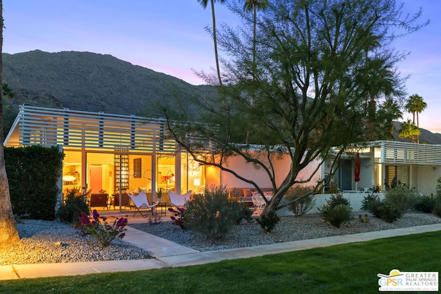 back house at dusk featuring a mountain view and a patio