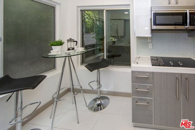 kitchen with black electric stovetop, light tile patterned floors, and backsplash